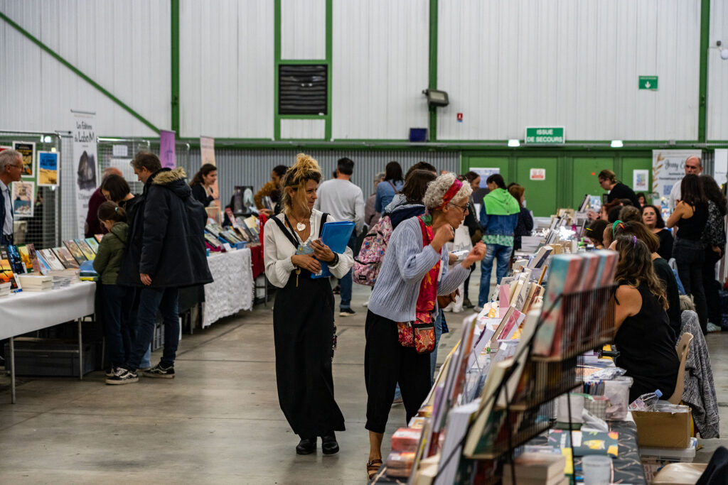 Foule de visiteurs explore un salon de livres avec des stands et des échanges entre participants.